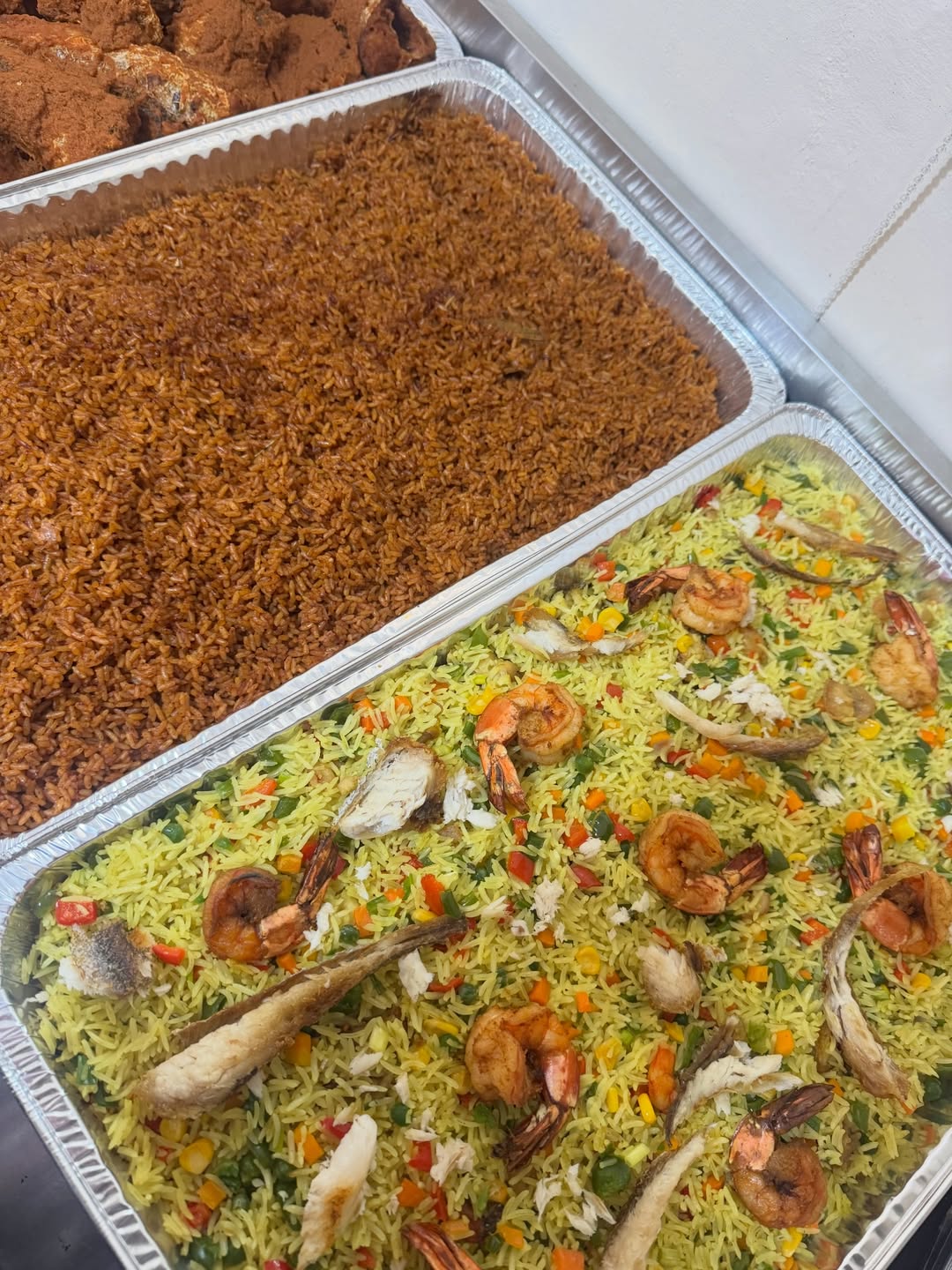 Large catering trays of jollof and fried rice with shrimp