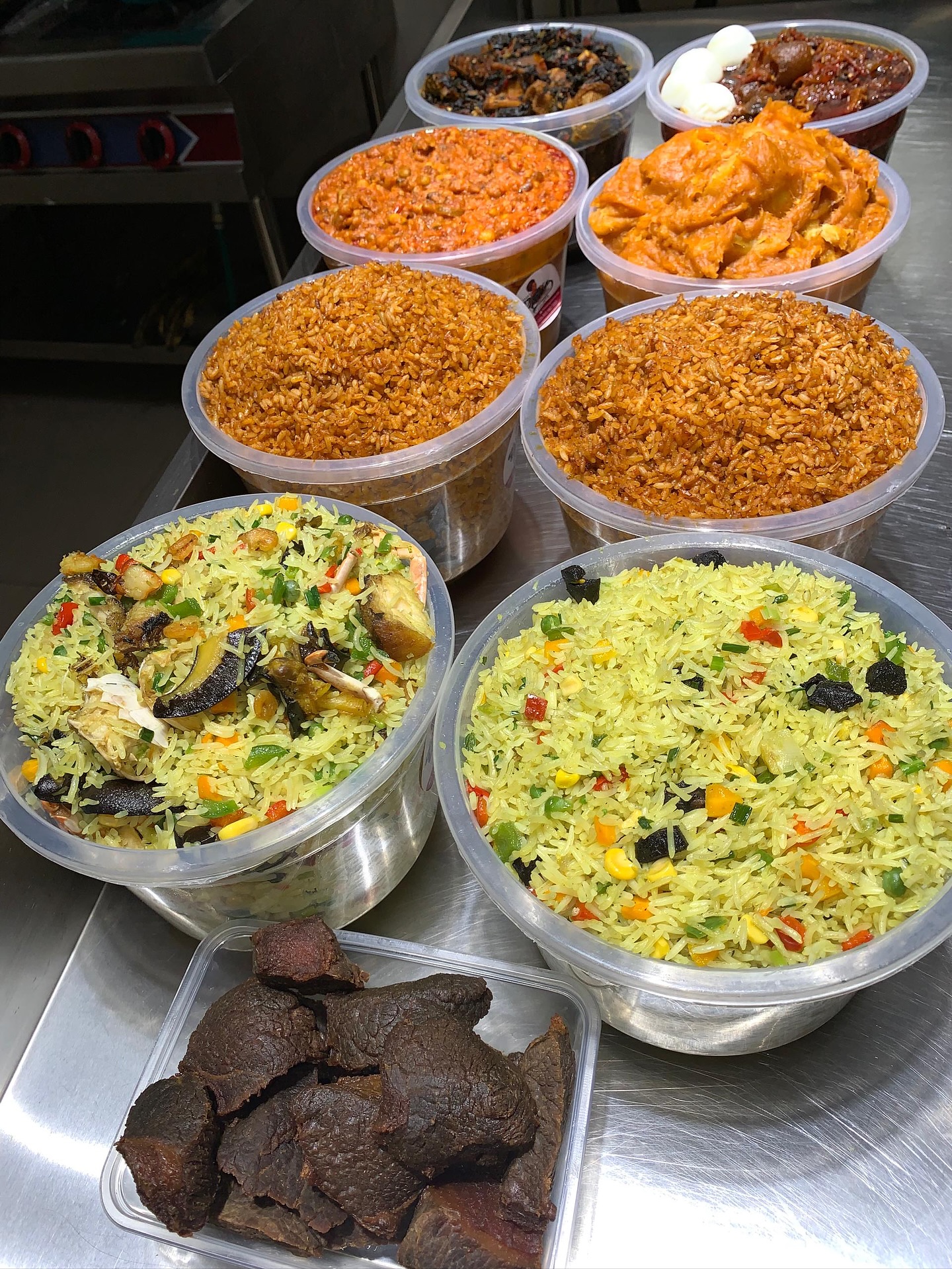 Kitchen spread — fried rice and jollof rice in large bowls with kilishi and assorted proteins