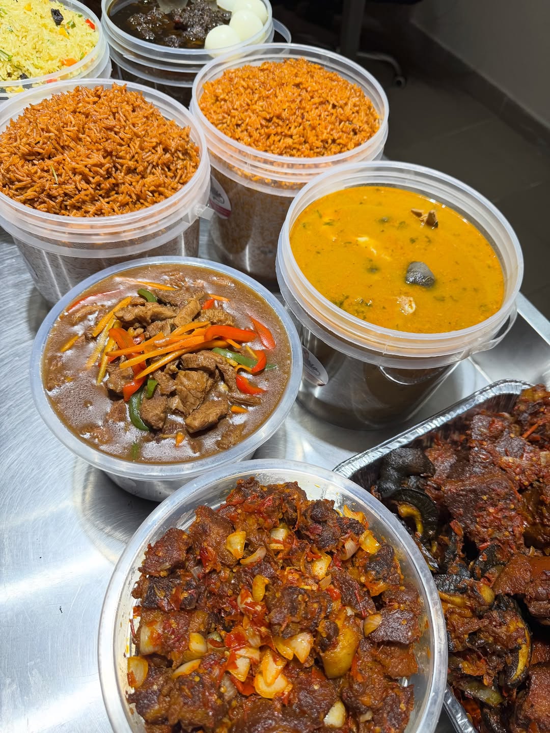 Assorted proteins — pepper beef, peppersoup, jollof and fried rice — in kitchen containers