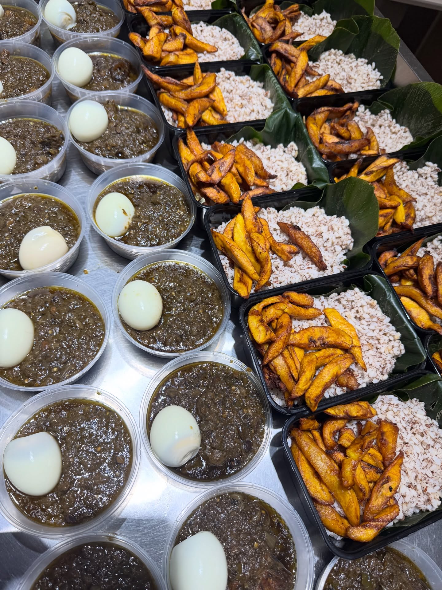 Rows of fresh ofada rice packs with ayamase stew and fried plantain on banana leaf