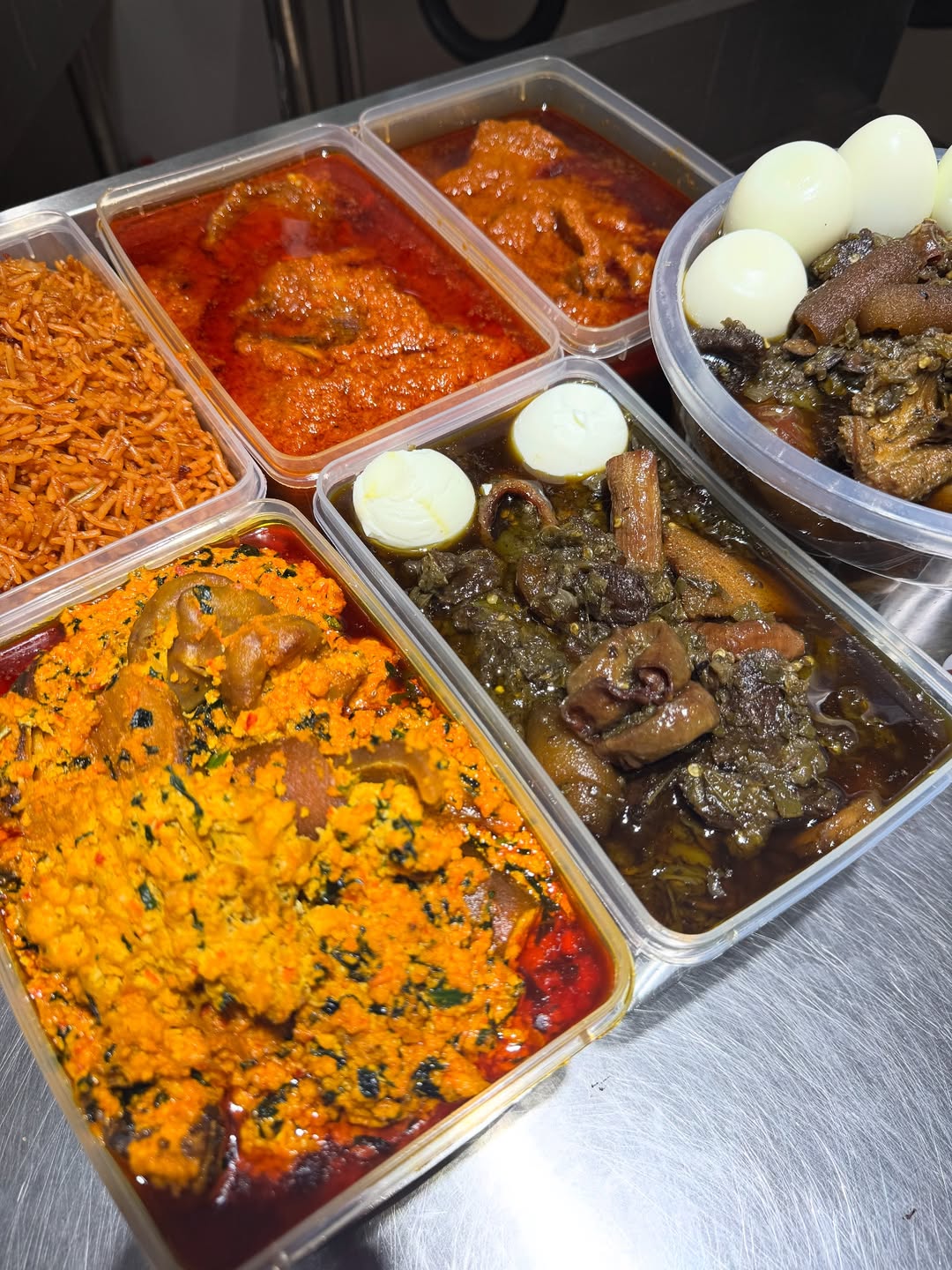 Full spread of ofada stew, jollof rice, fried rice, and assorted proteins in containers